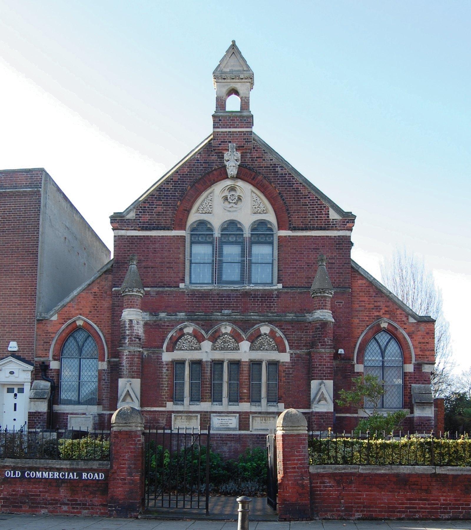 The front of the masjid on Old Commercial Road, behind its gate piers and railings