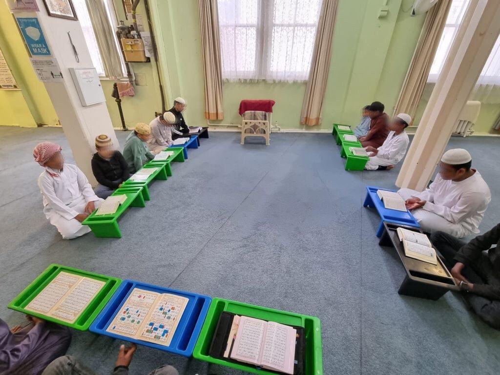 Boys reading Qur'an on green rehals in a circle on the masjid carpet