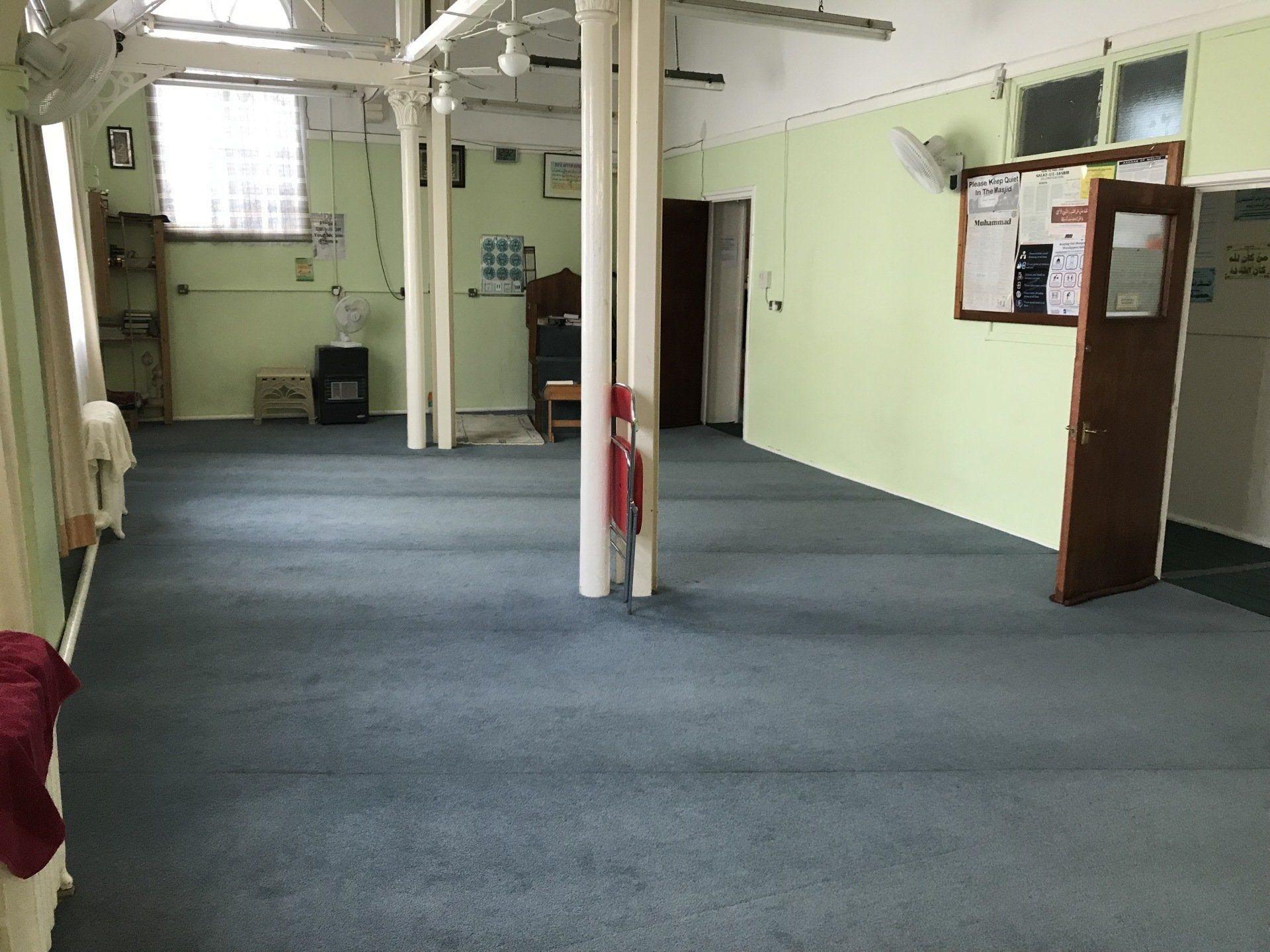 The empty prayer hall with its grey carpet, white pillars and green walls
